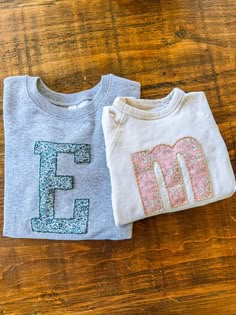 two t - shirts with the letters e and f on them sitting on a wooden surface