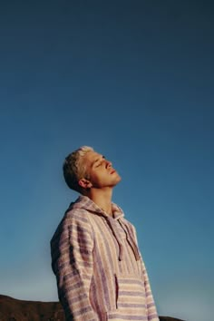 a man standing in front of a blue sky with his eyes closed and head tilted to the side