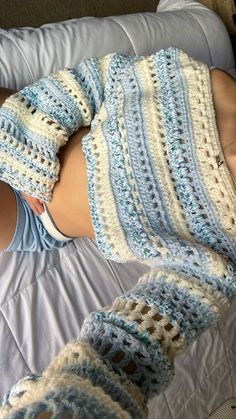 a woman laying on top of a bed covered in blue and white crochet