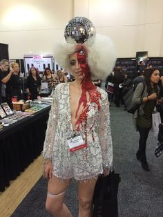 a woman dressed up as a disco dancer in a convention hall with people around her