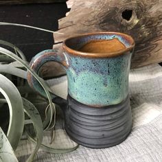 a coffee mug sitting on top of a table next to a plant and wood planks