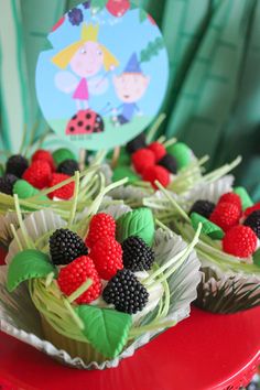 cupcakes decorated with raspberries and blackberries are on a red plate