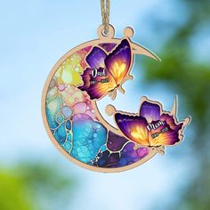 two butterflies sitting on top of a crescent shaped sun catcher with the word mom written on it