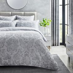 a bedroom with a large bed covered in grey and white comforter sets next to a window