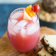 a drink with a cherry garnish sitting on top of a wooden cutting board