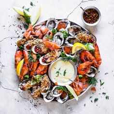 a platter filled with assorted seafood on top of a white countertop next to two small bowls of sauces