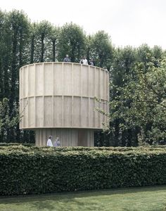 three people sitting on top of a round structure in the middle of a hedged area