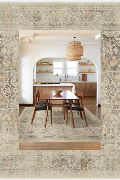 a dining room table and chairs in front of a kitchen with an archway leading into the living room