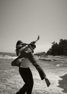 black and white photograph of two people on the beach, one holding the other in the air