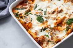 a casserole dish with meat, cheese and spinach leaves on the side