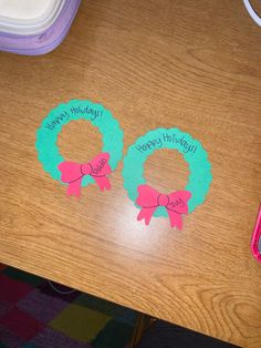 two paper wreaths sitting on top of a wooden table next to a pink pen