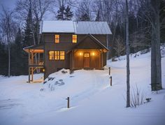 a cabin in the woods is lit up at night with snow on the ground and trees around it