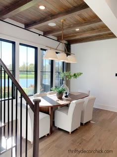 a dining room table with chairs and a vase on top of it in front of large windows