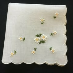 small white flowers and green leaves are placed on the edge of a linen napkin with scalloped edges