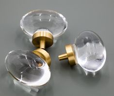 three glass door knobs with brass handles on a gray surface, one has a clear facet and the other is an oval