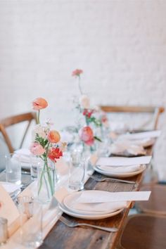 the table is set with white plates and pink flowers in glass vases on them