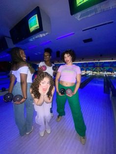 four women standing around bowling balls in a bowling alley