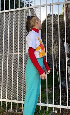 a woman standing in front of a white fence wearing blue pants and a pokemon t - shirt