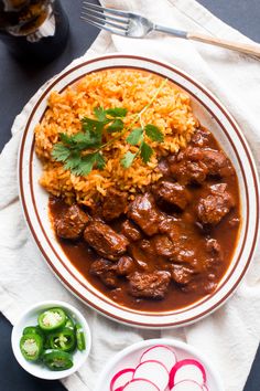 a white plate topped with meat and rice next to a bowl of green peppers on top of a table