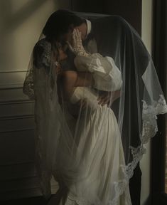 a bride and groom kissing in front of a window with veils over their heads