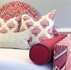 a bed topped with lots of pillows next to a pillow on top of a headboard