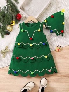 a green christmas tree dress with white shoes on the floor next to it and other holiday decorations