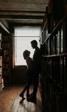 two people standing next to each other in front of a book shelf filled with books