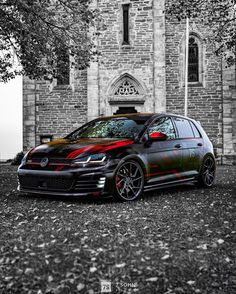 a black and red car parked in front of a brick building with a clock tower