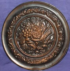 an ornate metal plate with grapes and flowers on it, sitting on a purple cloth