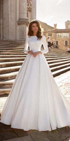 a woman in a white wedding dress standing on steps with her hands on her hips