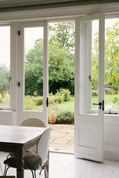 a table and chairs in front of large windows with doors open to the backyard area