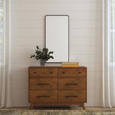 a wooden dresser with a mirror on top of it and a plant in front of it