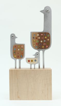 two metal birds standing on top of a wooden block