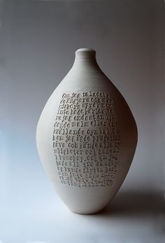 a white vase with writing on it sitting in front of a gray background and light