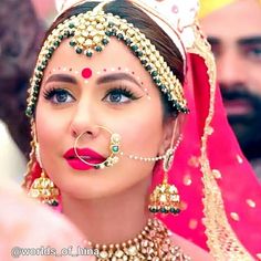 a woman in a red and gold outfit with jewelry on her head, wearing a tiara