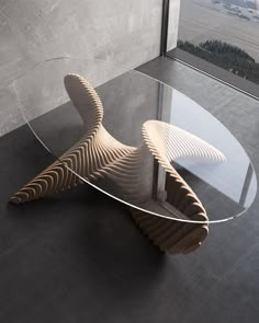 a glass table with an unusual wooden design on the top and bottom, in front of a large window