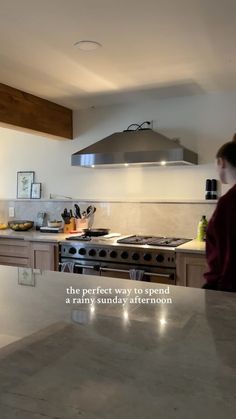 a woman standing in a kitchen next to a stove top oven and counter with an advertisement on it