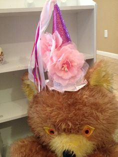 a brown teddy bear with a pink flower on it's head sitting in front of a shelf