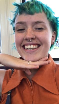 a woman with green hair and piercings on her nose smiles at the camera while wearing an orange shirt