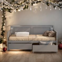 a white bed sitting under a christmas tree next to a wall with lights on it