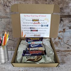 an open box with some candy and pencils in it on a wooden table next to a tin can