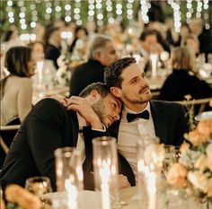 two men in tuxedos sitting at a dinner table