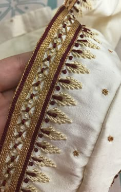 a hand is holding a piece of cloth with gold trimmings and beads on it