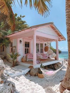 a small pink house on the beach with hammock and palm trees in front