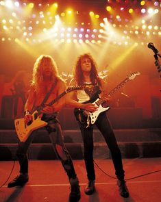 two people on stage with guitars in their hands and one person holding an electric guitar