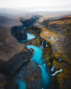 an aerial view of a river running through a valley surrounded by rocky cliffs and green grass