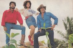 two men and a woman standing on top of a rock in front of some plants