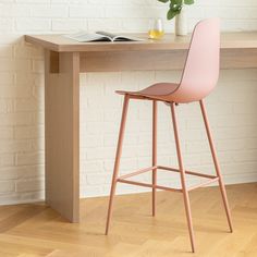 a pink bar stool sitting in front of a wooden table with a book on it