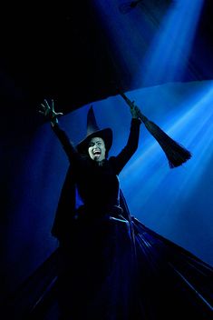 a woman dressed as a witch with her arms in the air and holding an umbrella