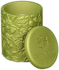 a green candle holder with a cross and leaves design on the front, sitting next to it's lid